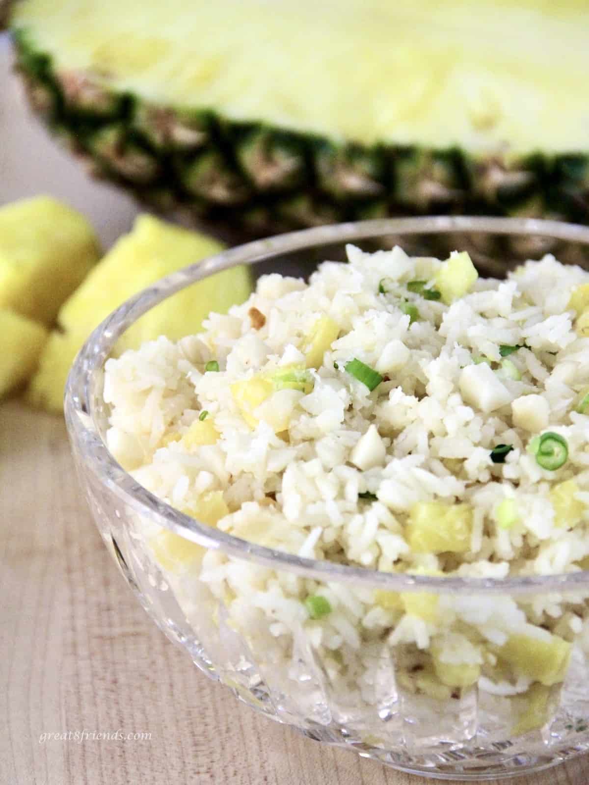 Upclose view of pineapple rice in a glass bowl with fresh pineapple in the background.