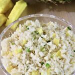 Glass bowl of pineapple rice salad with some chunks of pineapple in the background.