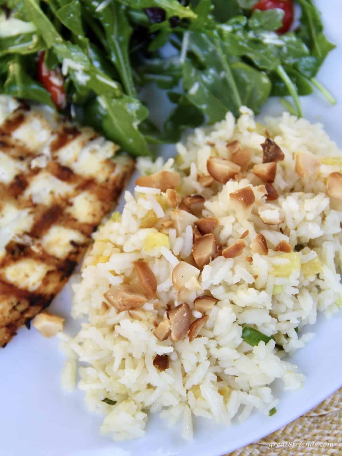 Dinner plate with a rice salad including pineapple and sprinkled with toasted macadamia nuts with a small piece of white fish and a salad on the side.