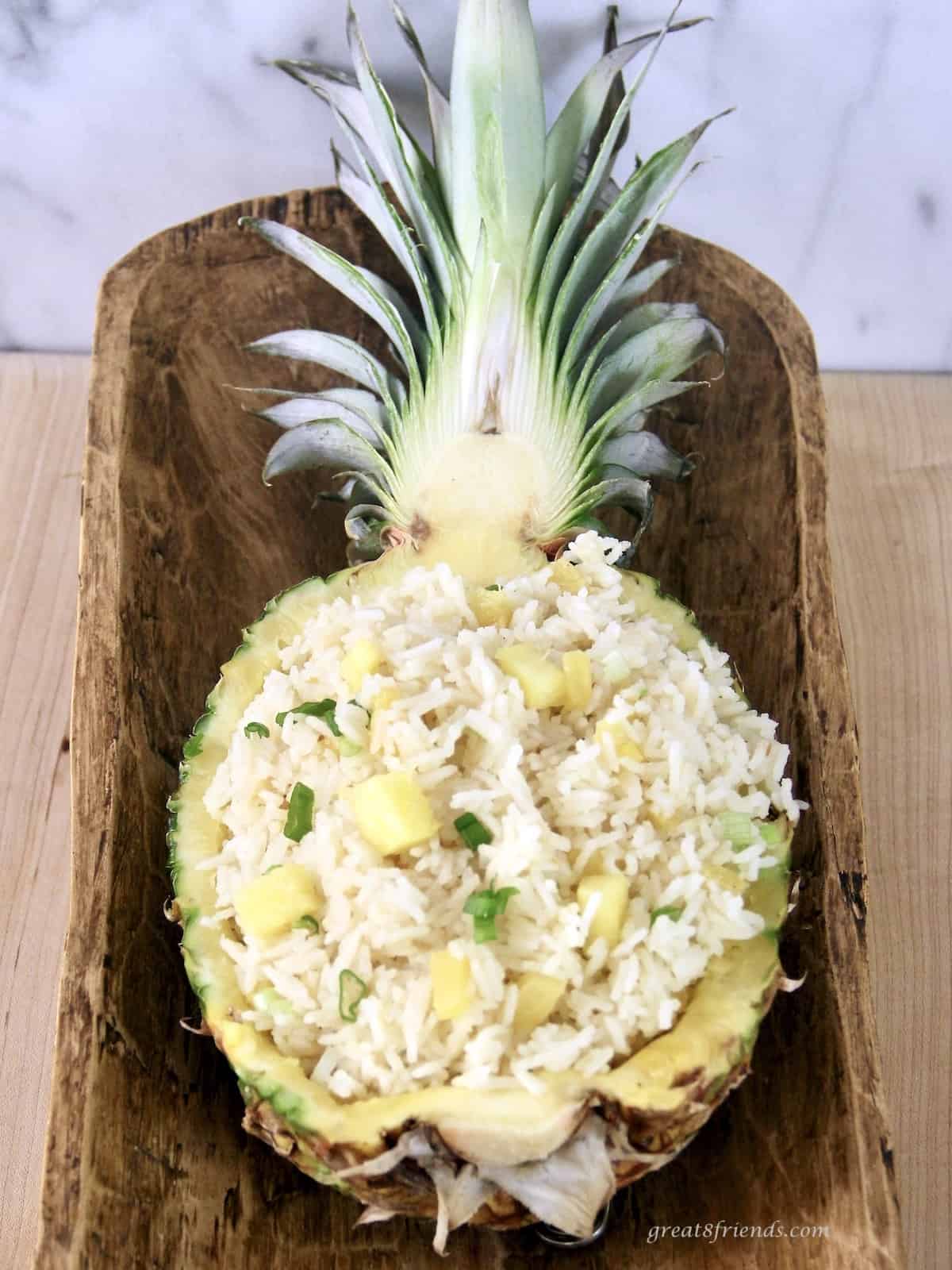 Pineapple Rice Salad being served in a fresh pineapple shell in a wooden boat shaped bowl.