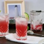 Two crystal glasses with Nantucket Breeze cocktail garnished with lime wedges. a mixing glass in the background.