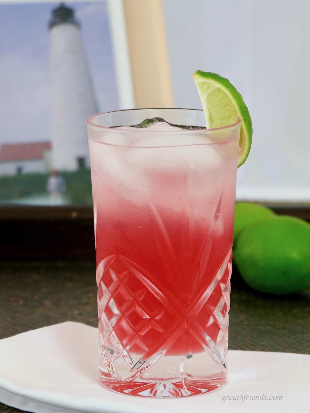 Photo of a red cocktail in a highball glass garniished with a wedge of lime.