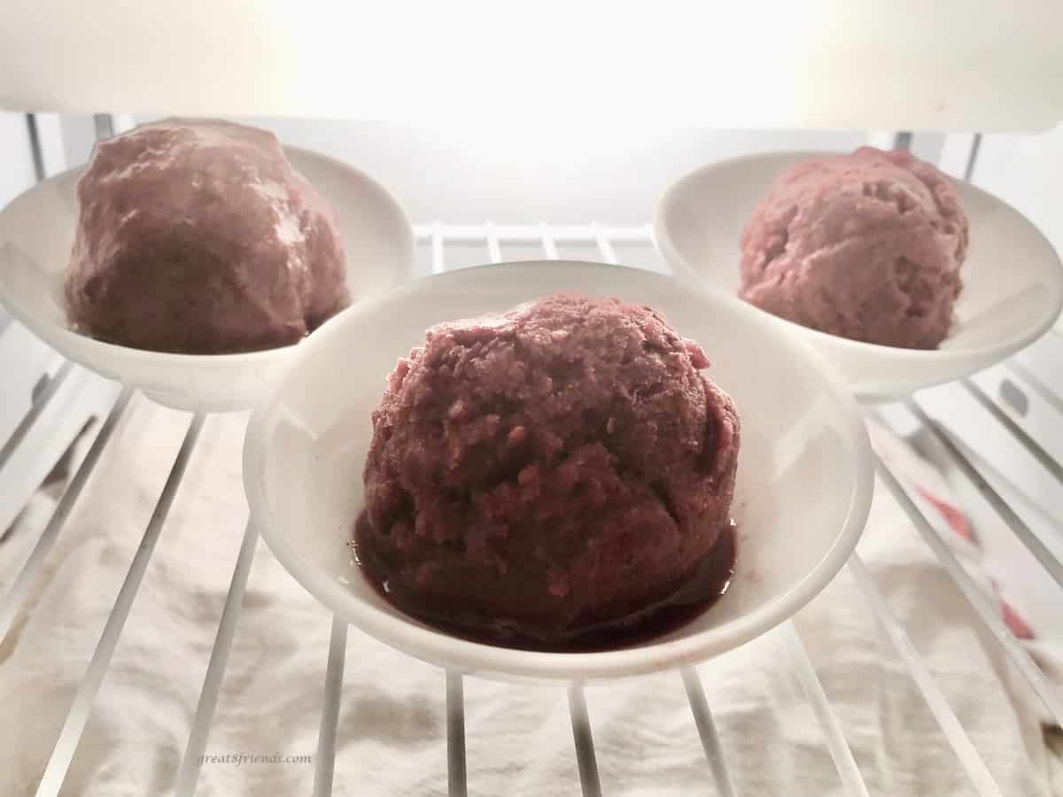 Three scoops of blackberry ice each in a small white bowl in the freezer.