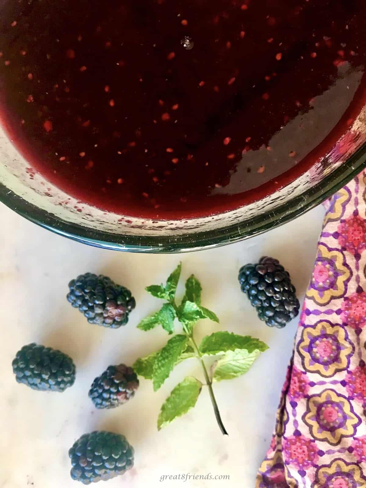 Cooked berries in a glass bowl with fresh blackberries and a sprig of mint on the side.