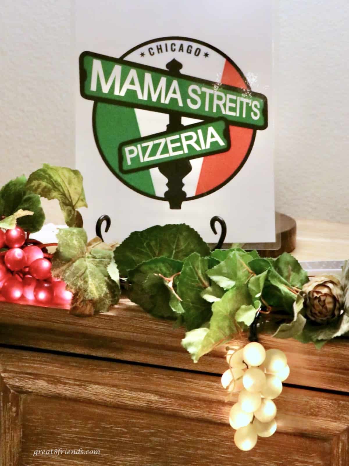 Mama Streit's Pizzeria sign on a mantle with decorative green and red grapes with lights.