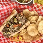 Slow Cooker Italian Beef Sandwich served with potato chips on a red and white serving paper.