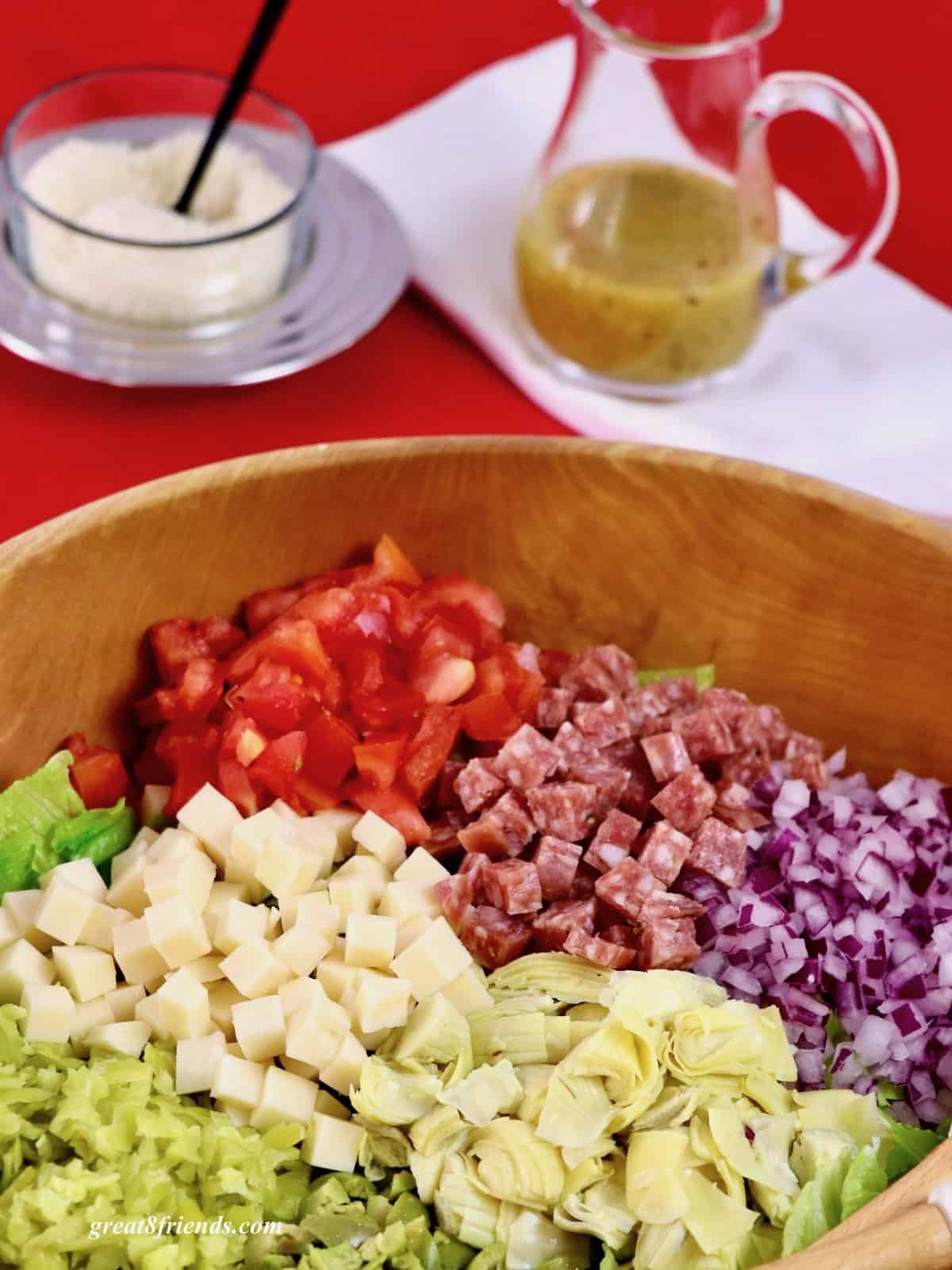 Wooden Salad Bowl with chopped tomatoes, salami, red onion, cheese, artichokes hearts, olives, and pepperoncini.