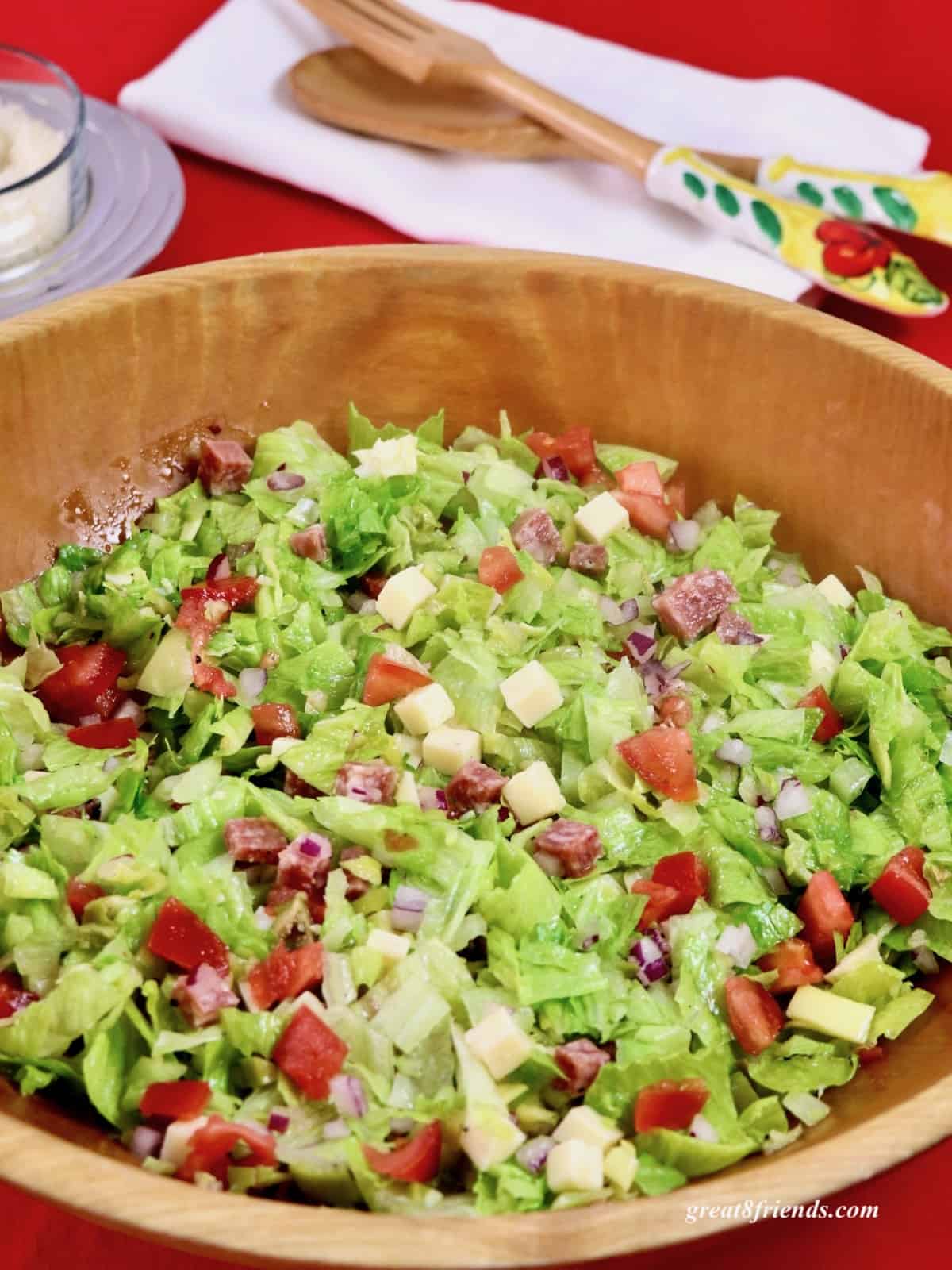 Italian Chopped Salad in a wooden bowl with salad servers in the background.