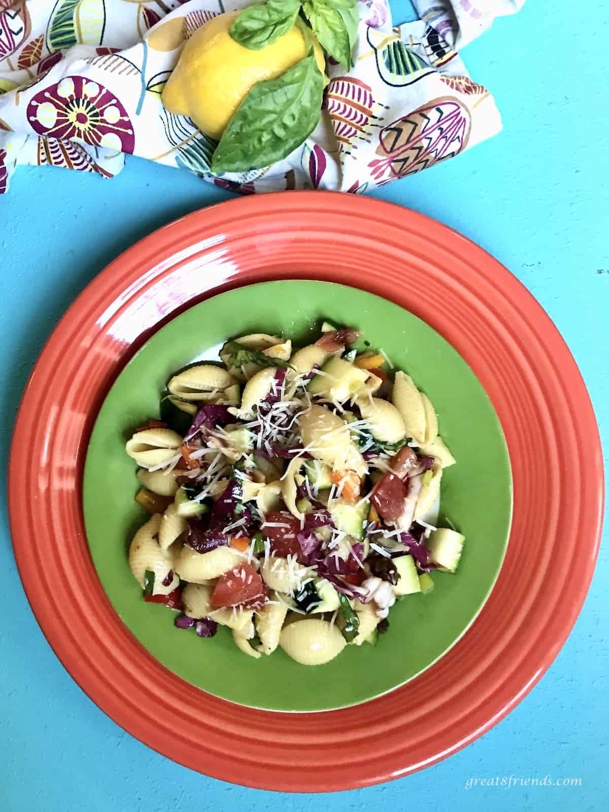 Shell pasta salad with vegetables on a green and red plate.