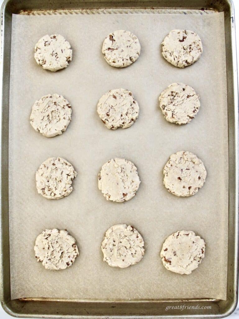 Twelve raw pecan cookies on a baking sheet.