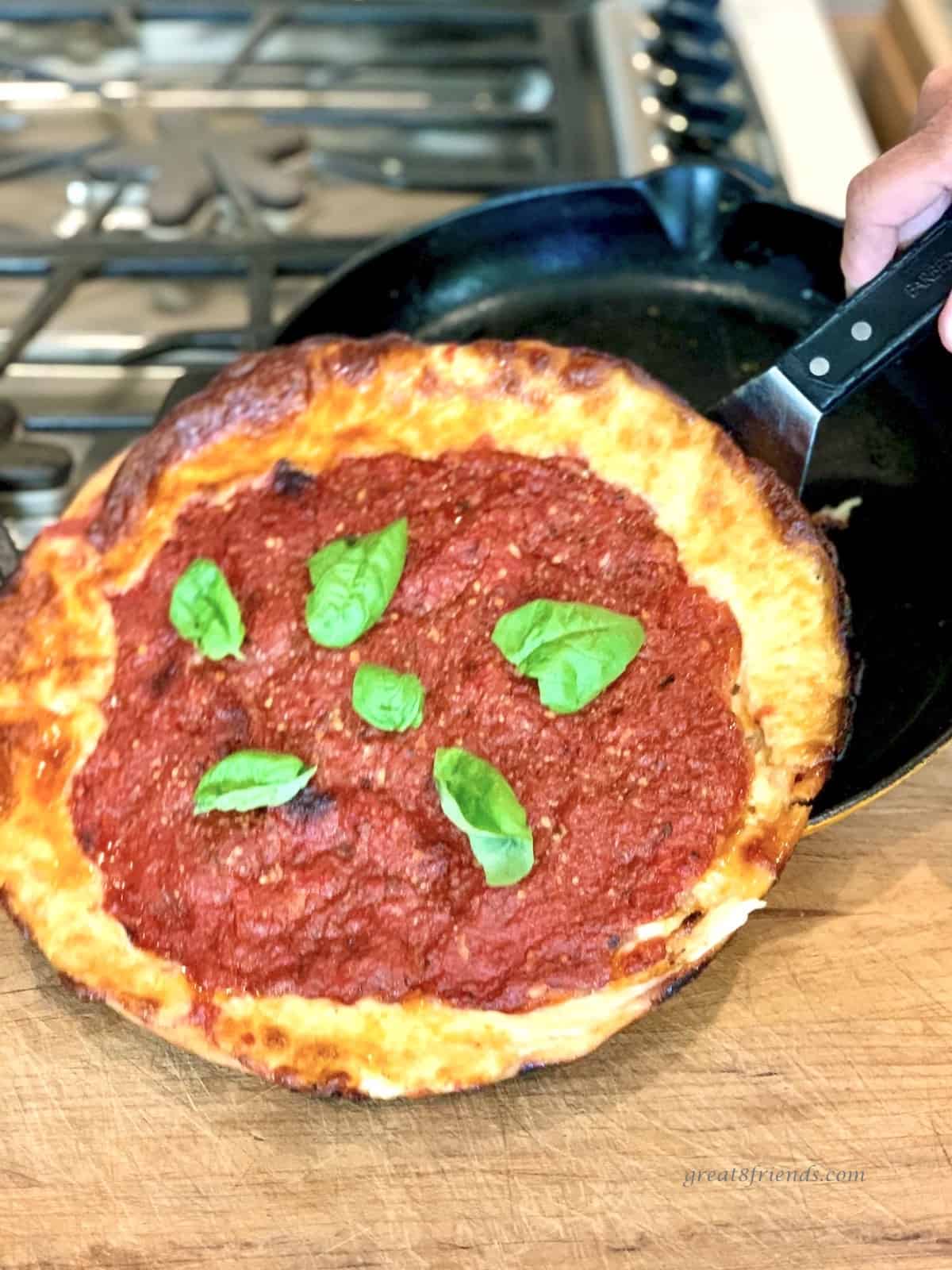 A whole Chicago pizza being slid out of a cast iron skillet with a spatula.