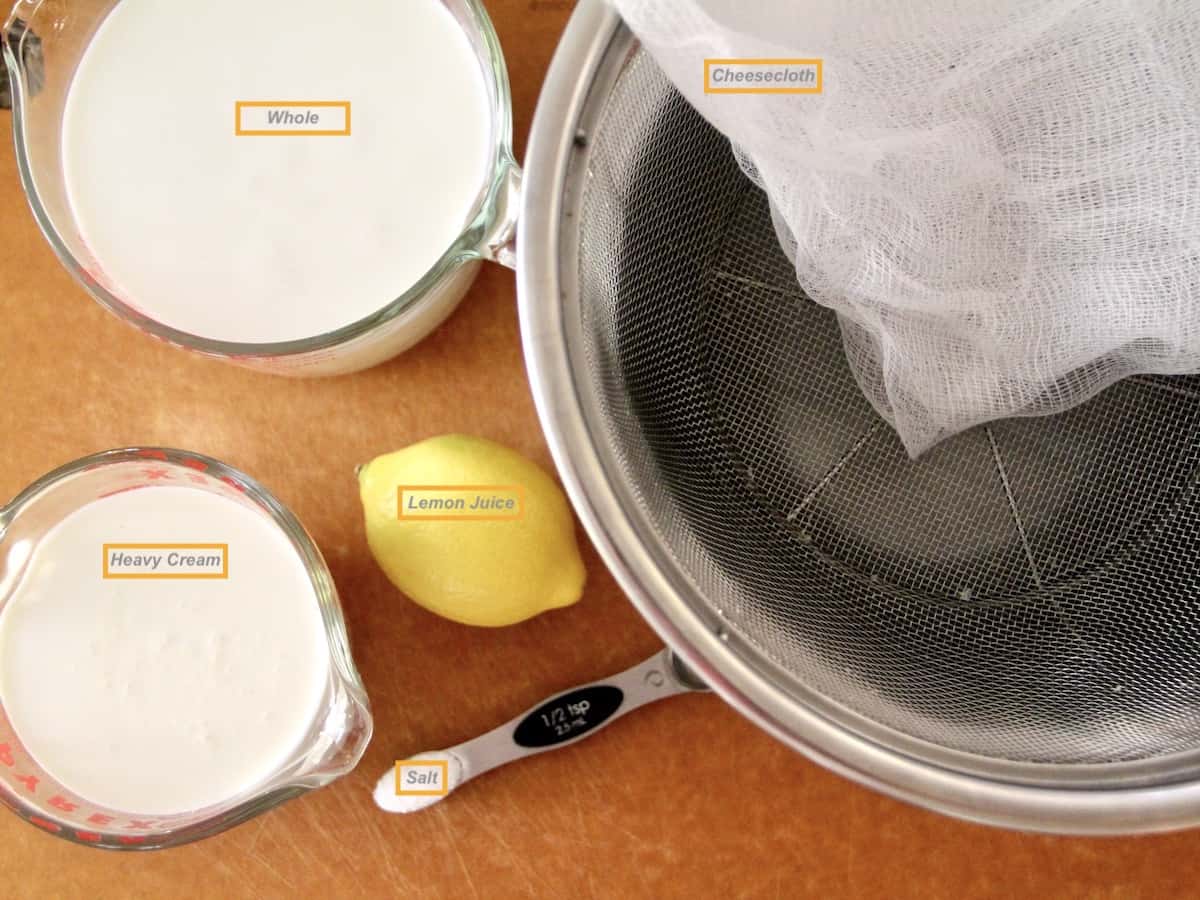 Ingredients needed for homemade ricotta. Milk, cream, lemon, and salt. Also showing a cheesecloth and strainer.