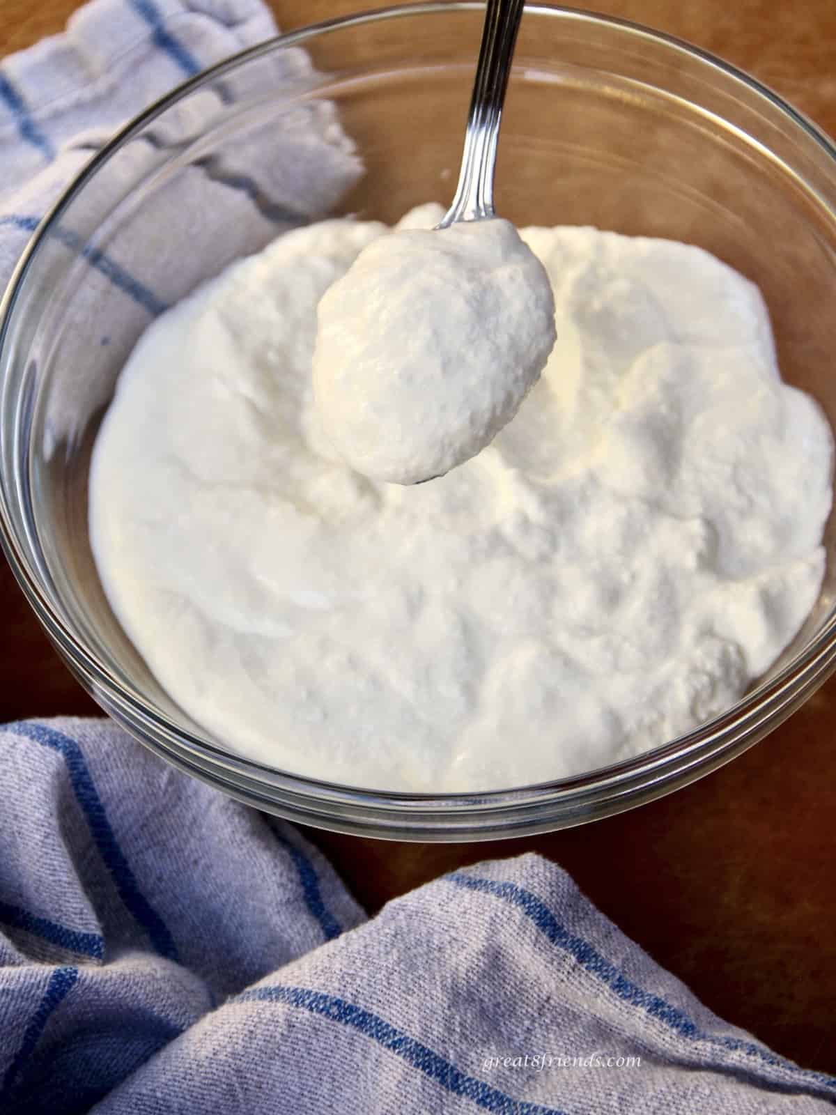 A spoonful of homemade ricotta cheese over a bowl of the cheese.