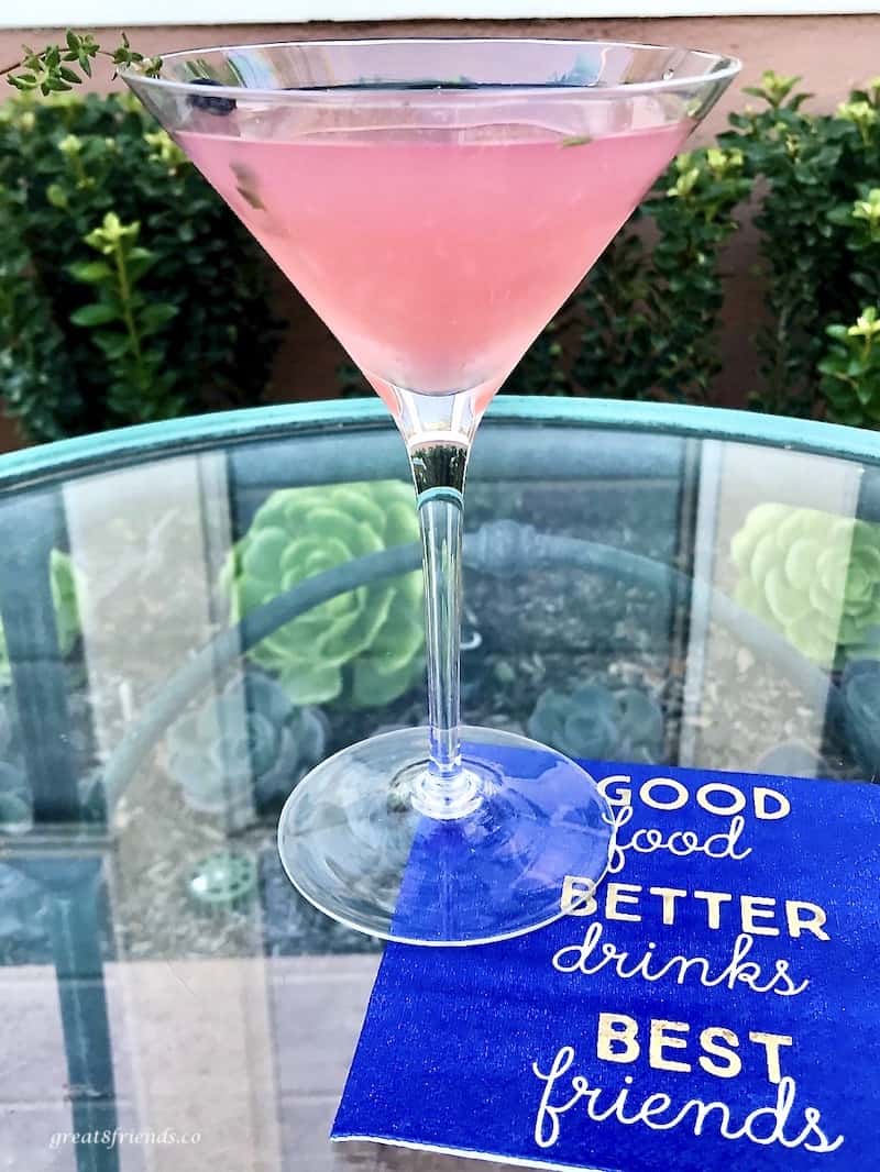 A thyme martini outside on a glass table with a royal blue napkin.