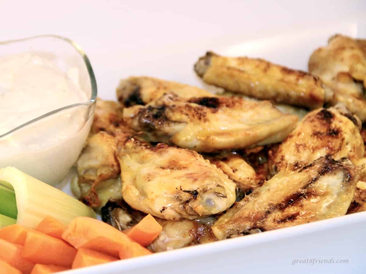 Buffalo chicken wings in a white dish served with dressing, carrots, and celery.