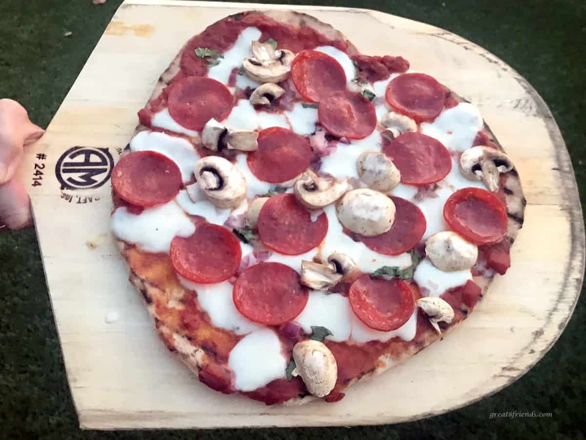 Grilled pizza with pepperoni, pizza sauce, cheese and mushrooms on a wood pizza board.