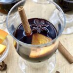 Glass cup with warm red wine garnished with a cinnamon stick, star anise and an orange slice.