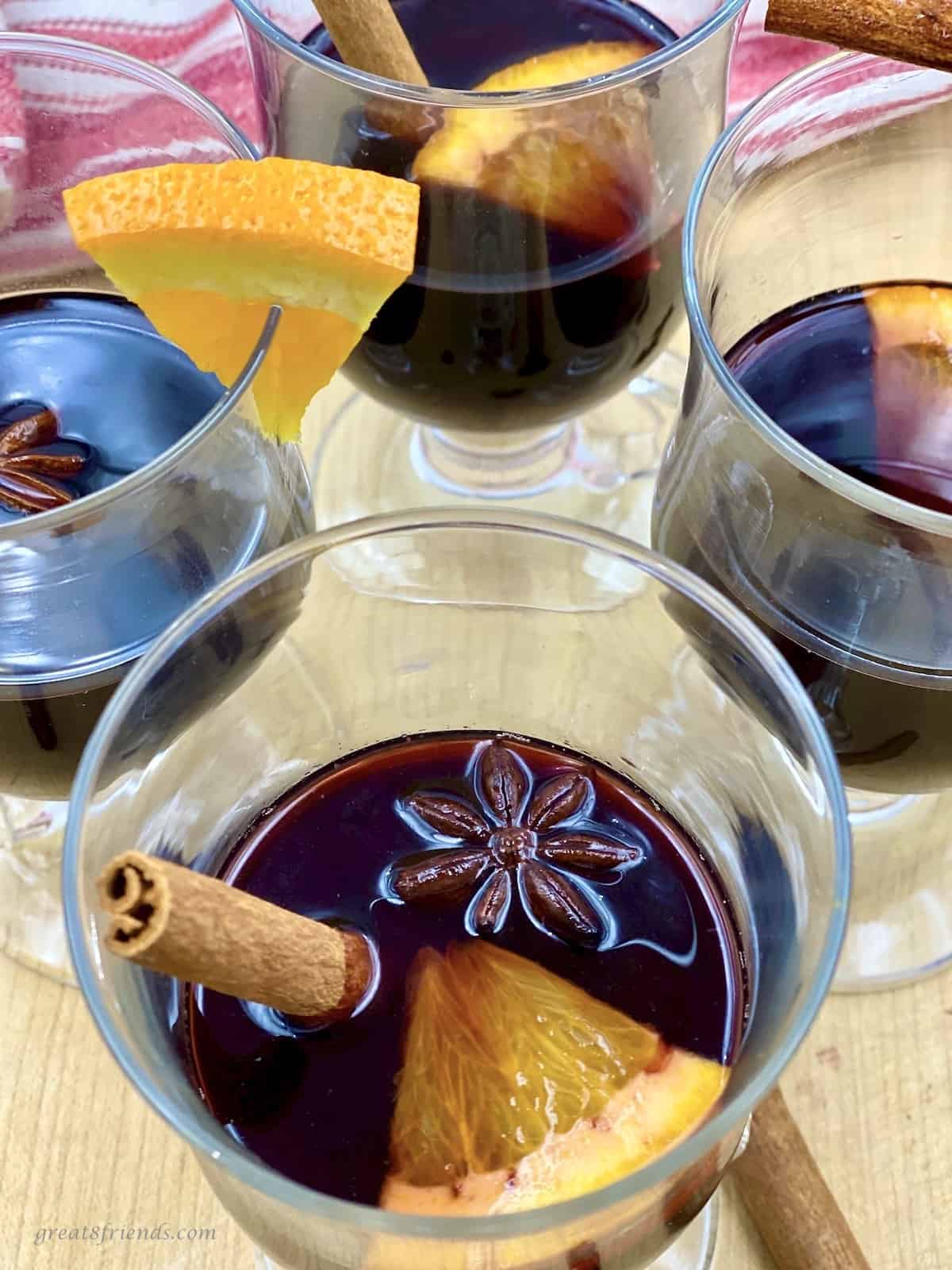 Four glass cups with mulled red wine garnished with cinnamon sticks and oranges slices.