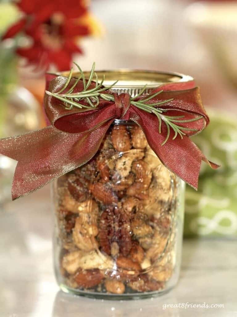 Rosemary spiced nuts in a mason jar with a red bow and rosemary sprig to decorate.