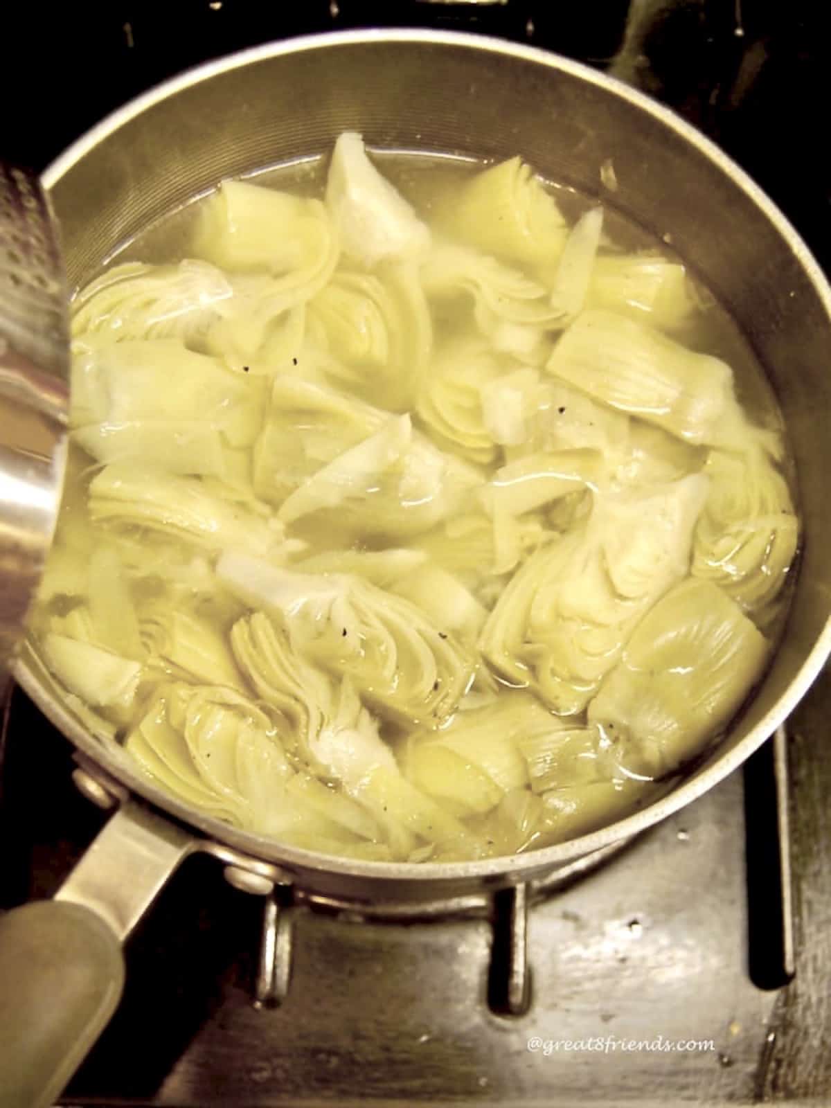 Artichokes simmering in a pan on a stove.