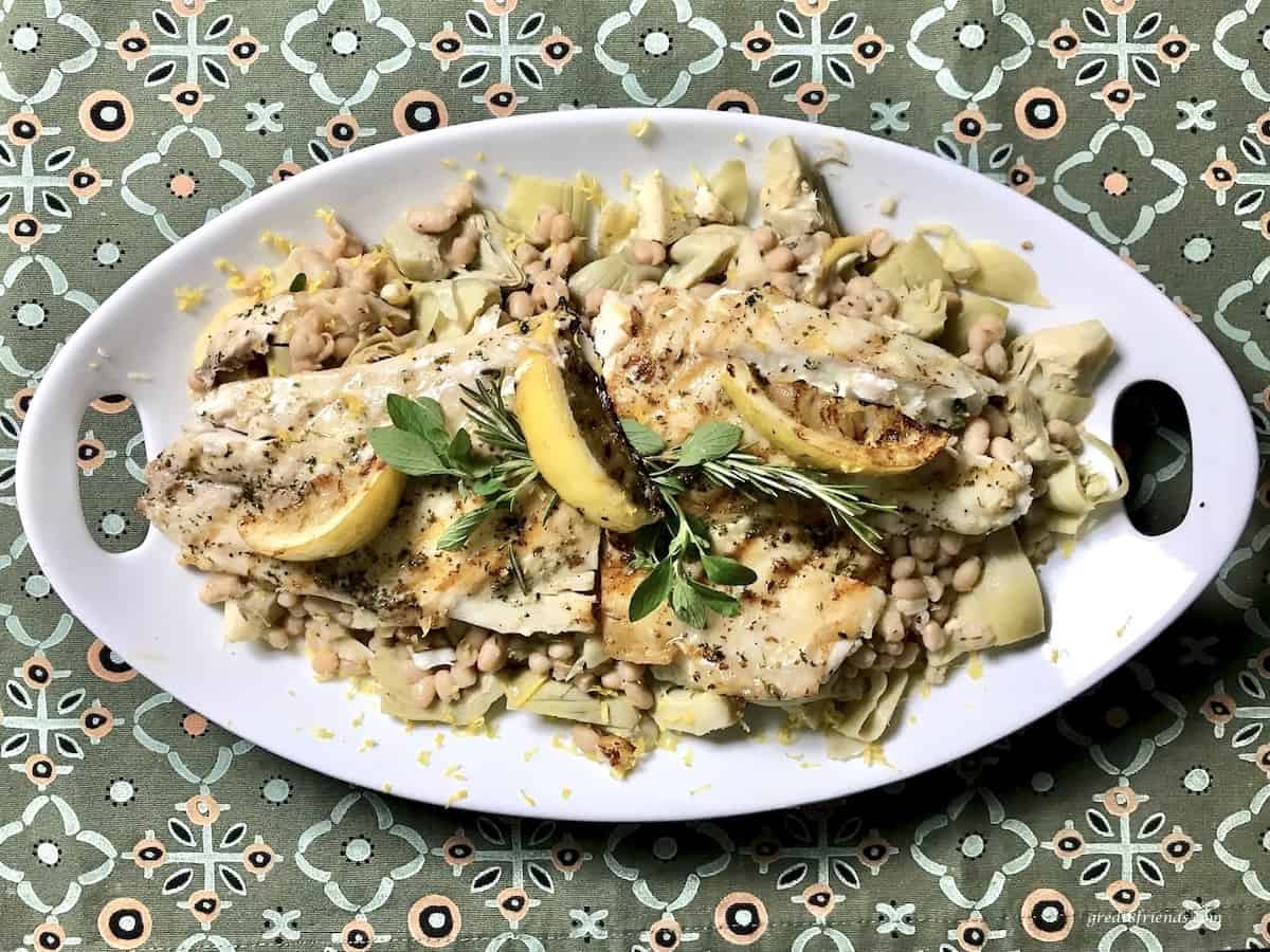 Sea bass with white beans and artichokes on an oval platter.