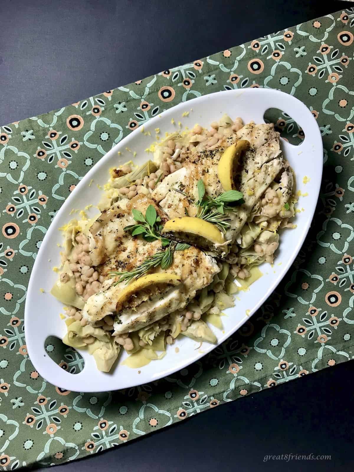 Sea bass with white beans and artichokes on an oval platter.