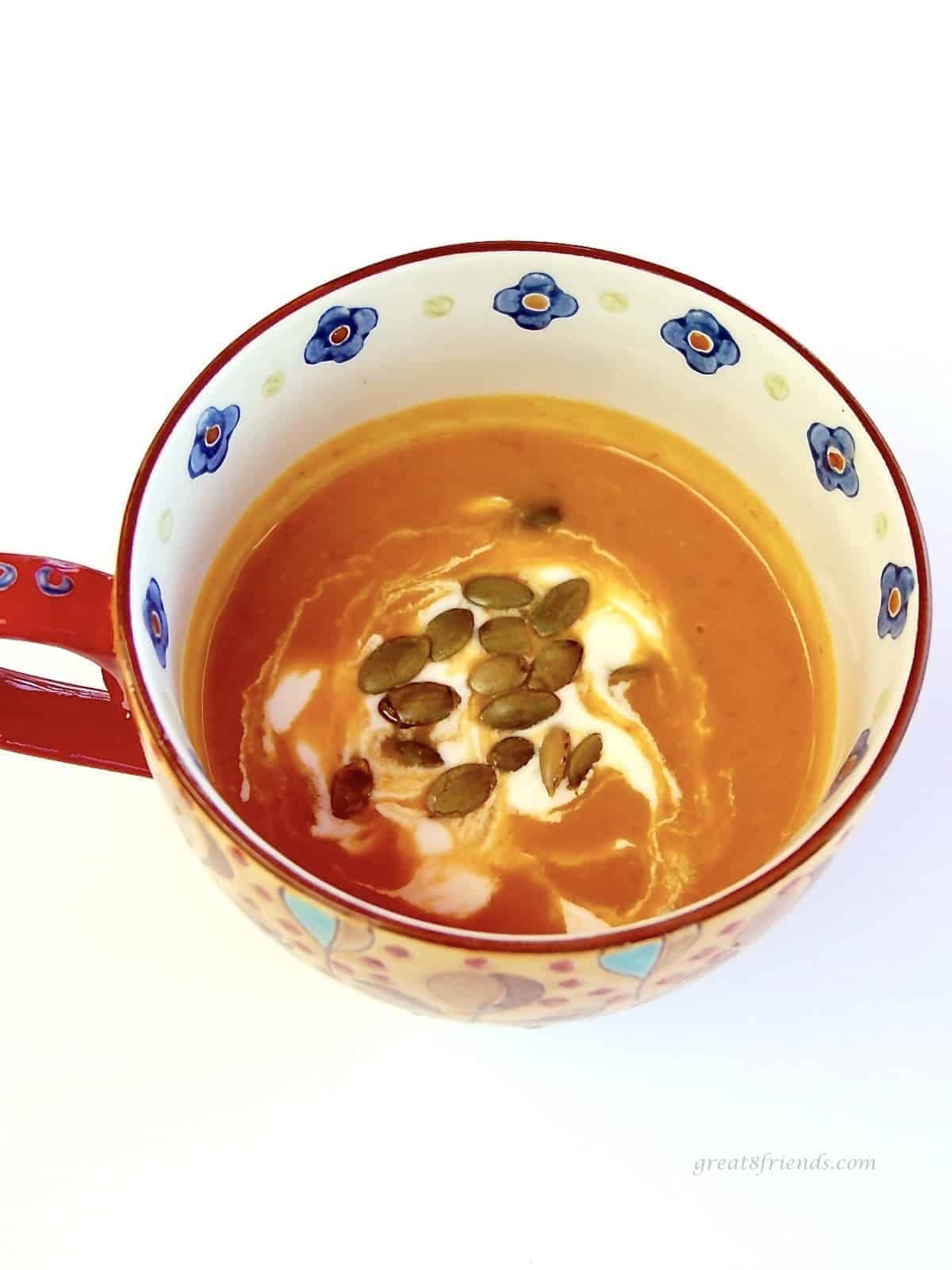 Colorful cup of pumpkin soup with crema and pepitas sprinkled on top.
