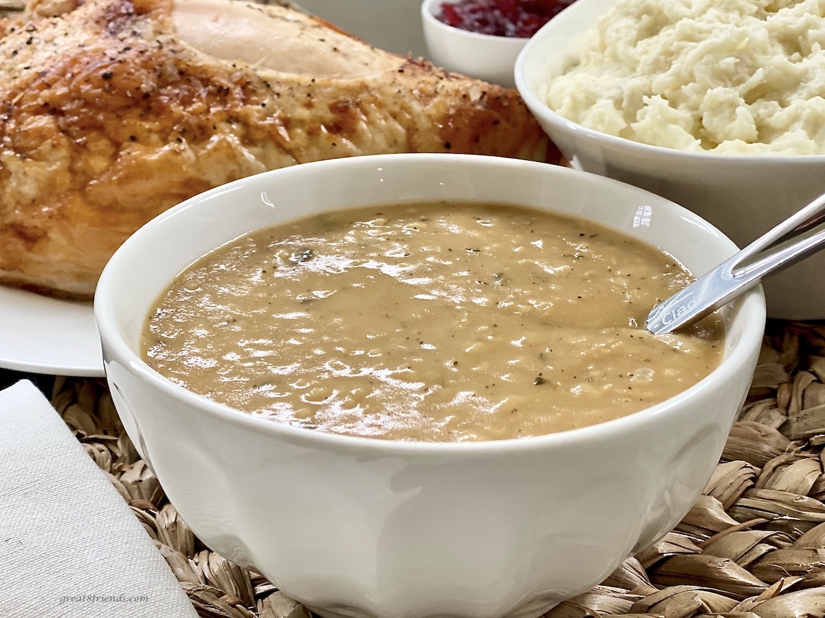 Gravy, turkey and mashed potatoes in white serving bowls.