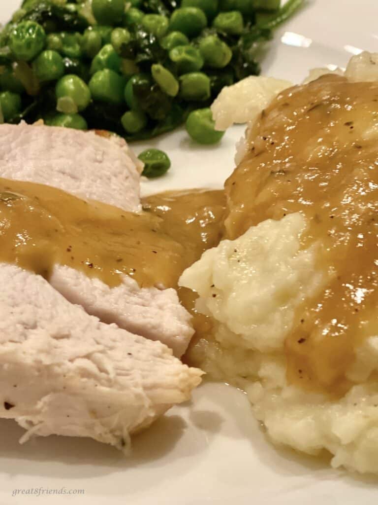 Sliced turkey, peas and mashed potatoes and gravy on a plate.