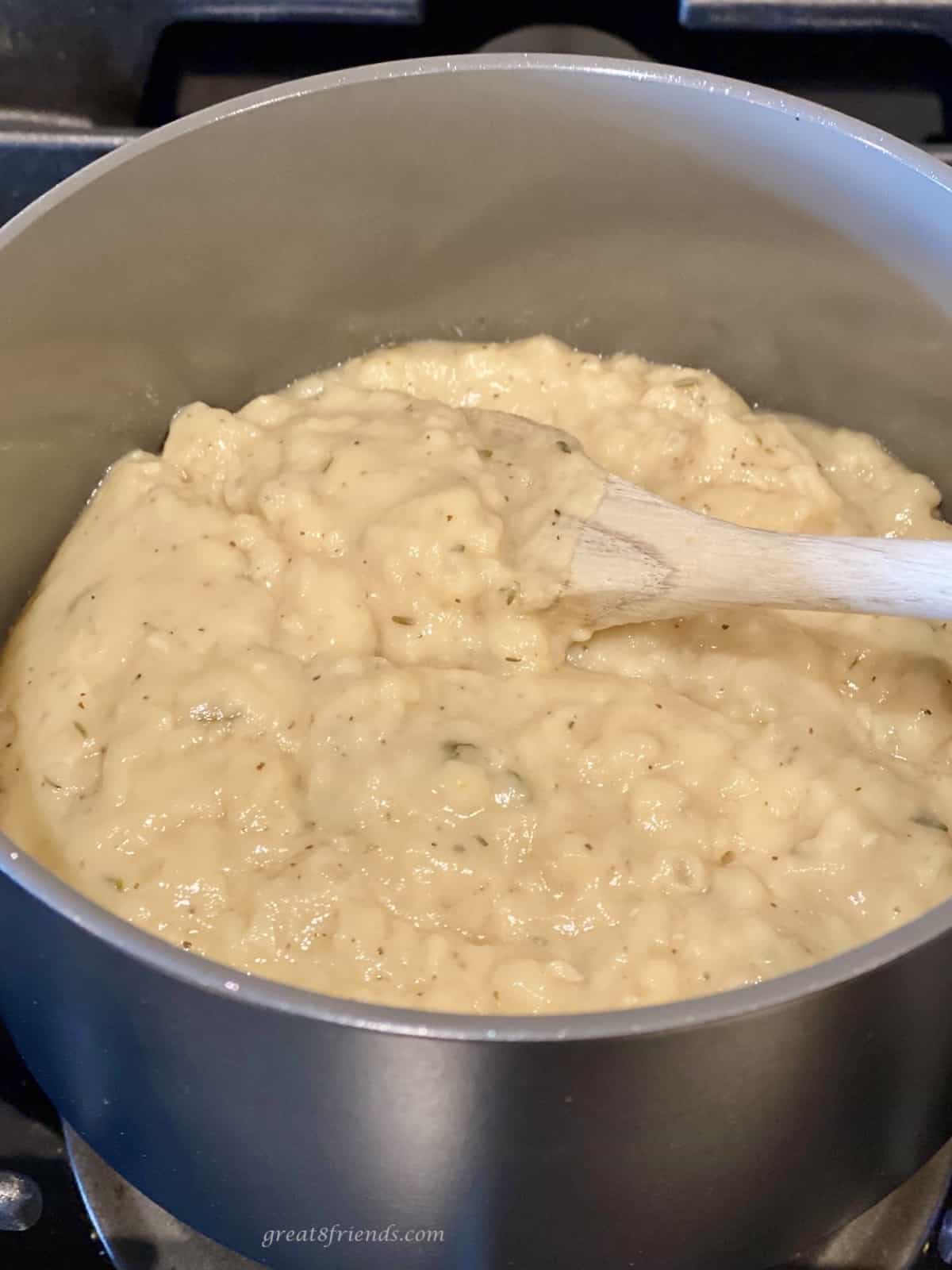 Chicken gravy being warmed on the stove in a stainless pot and being stirred with a wooden spoon.