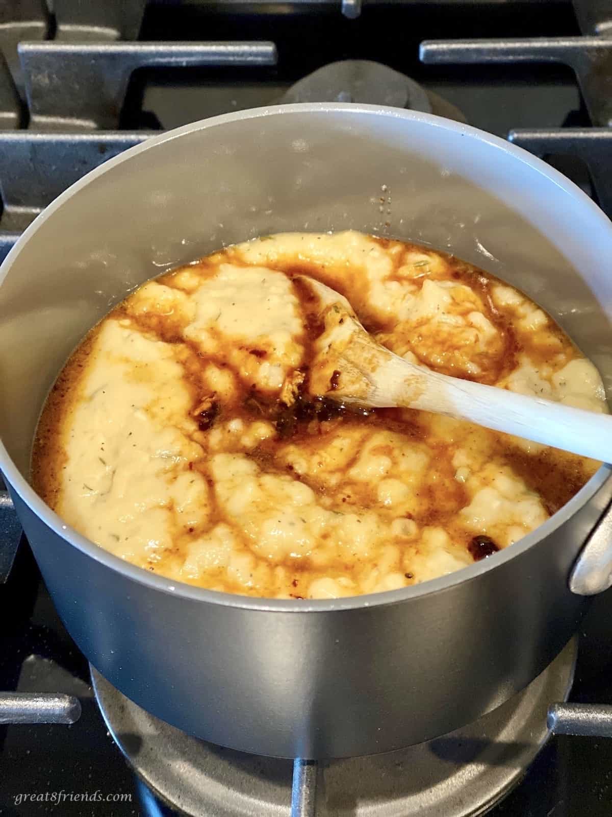 Gravy being warmed on the stove in a pot with the turkey drippings being stirred in with a wooden spoon.