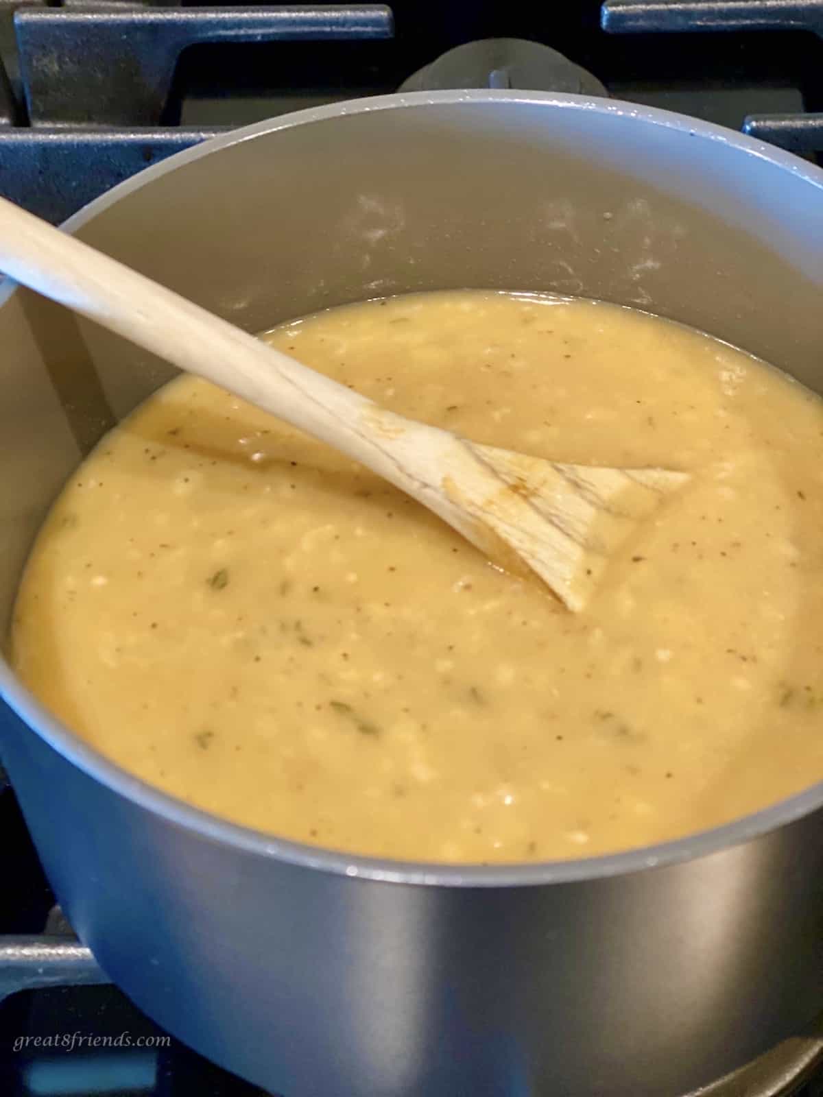 Brown sauce being warmed on the stove with a wooden spoon.