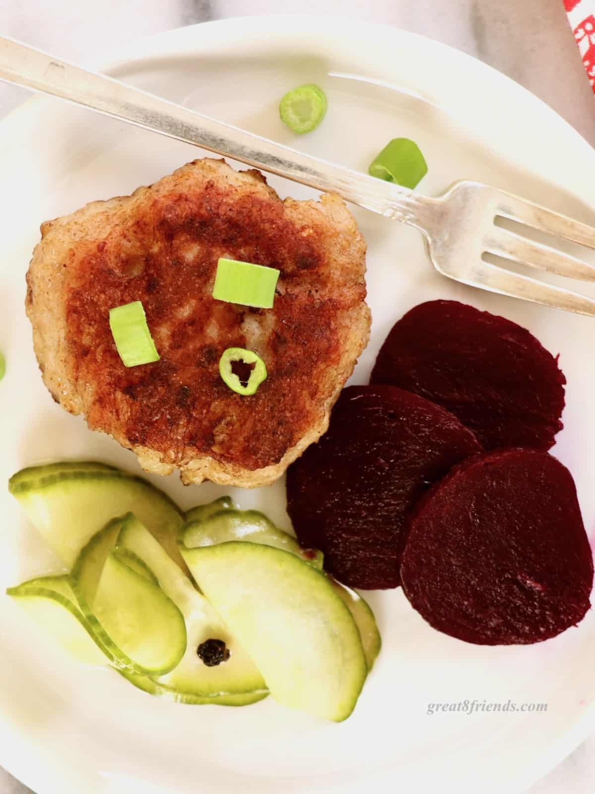 Overhead shot of one Danish meatball on a plate with a small fork, some pickled sliced pickled beets and cucumber salad.