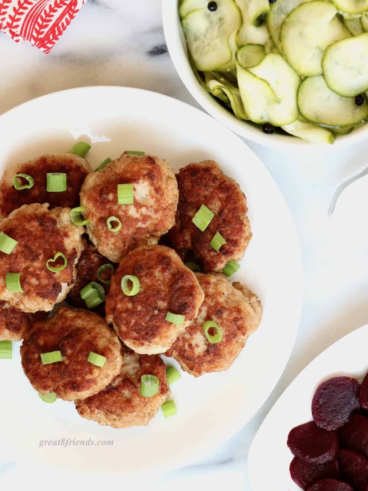 Overhead shot of Danish Meatballs stacked on a white plate sprinkled with cut green onion.