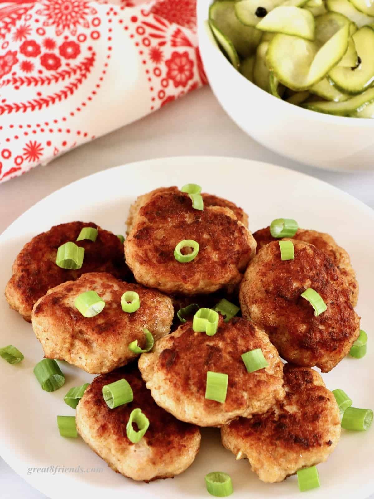 Danish meatballs stacked on a white plate garnished with cut green onion.