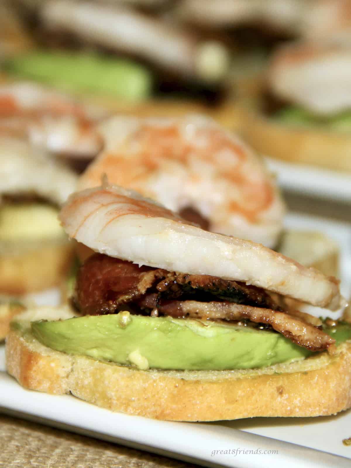 Unclose shot of a toasted piece of French bread with avocado, bacon and shrimp on top.