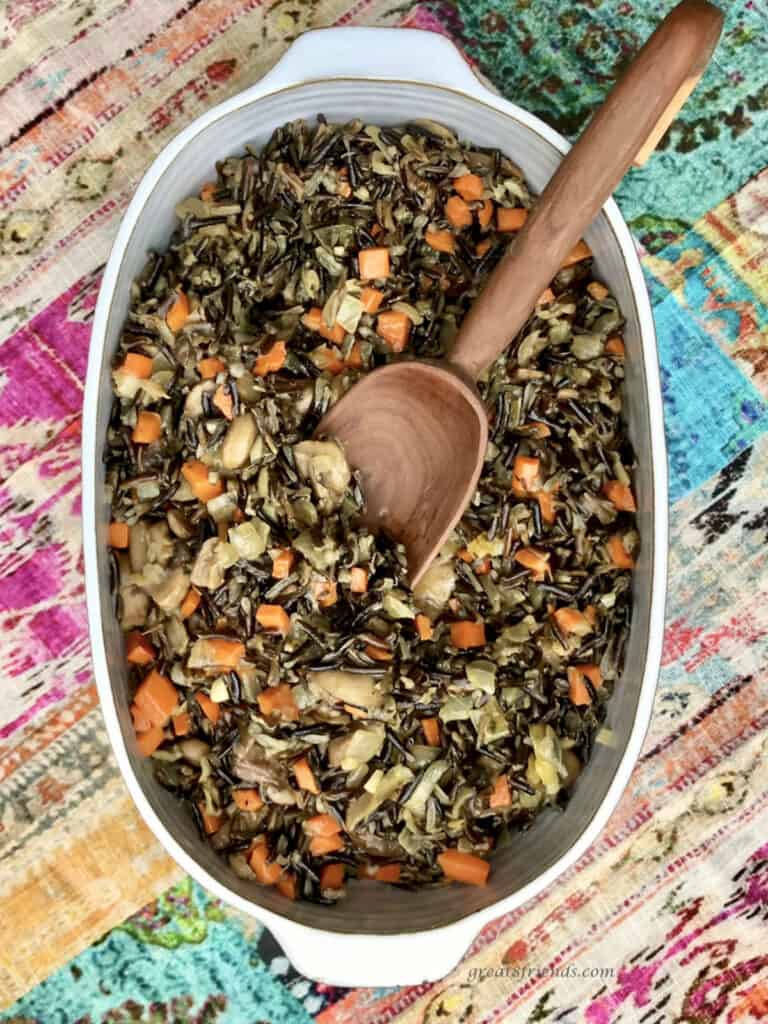 Wild Rice with mushrooms in a white baking dish being served from a wooden spoon.