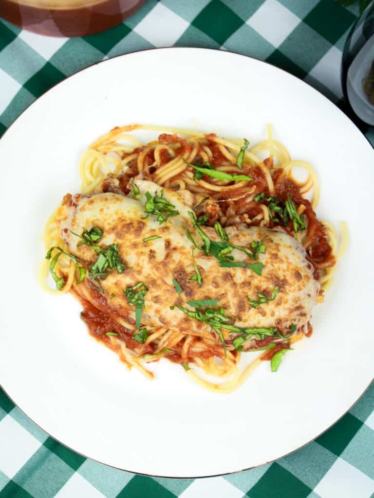 Overhead shot of Chicken Parma on a white plate garnished with parsley.