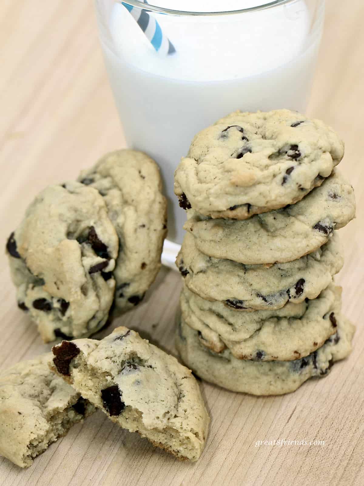 Chocolate chip cookies stacked on each other in front of a glass of milk.