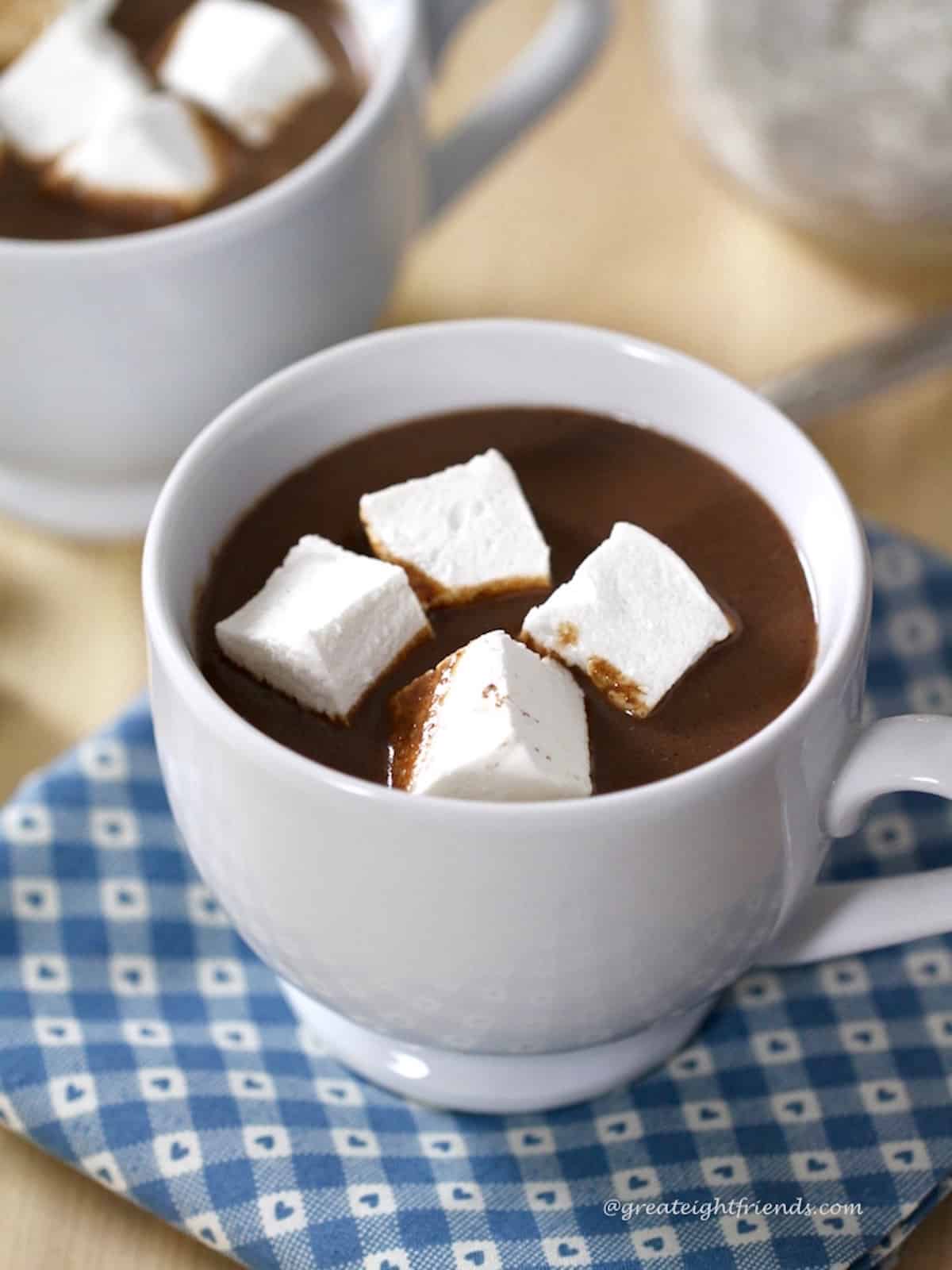 Homemade hot chocolate in a white mug with four white square marshmallows floating on top