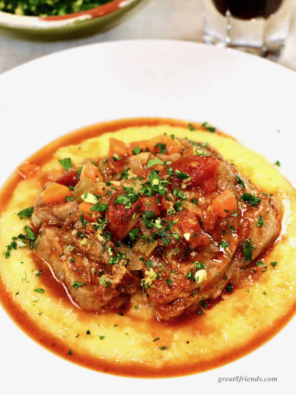 Osso buco on a bed of polenta in a white dish topped with gremolata.