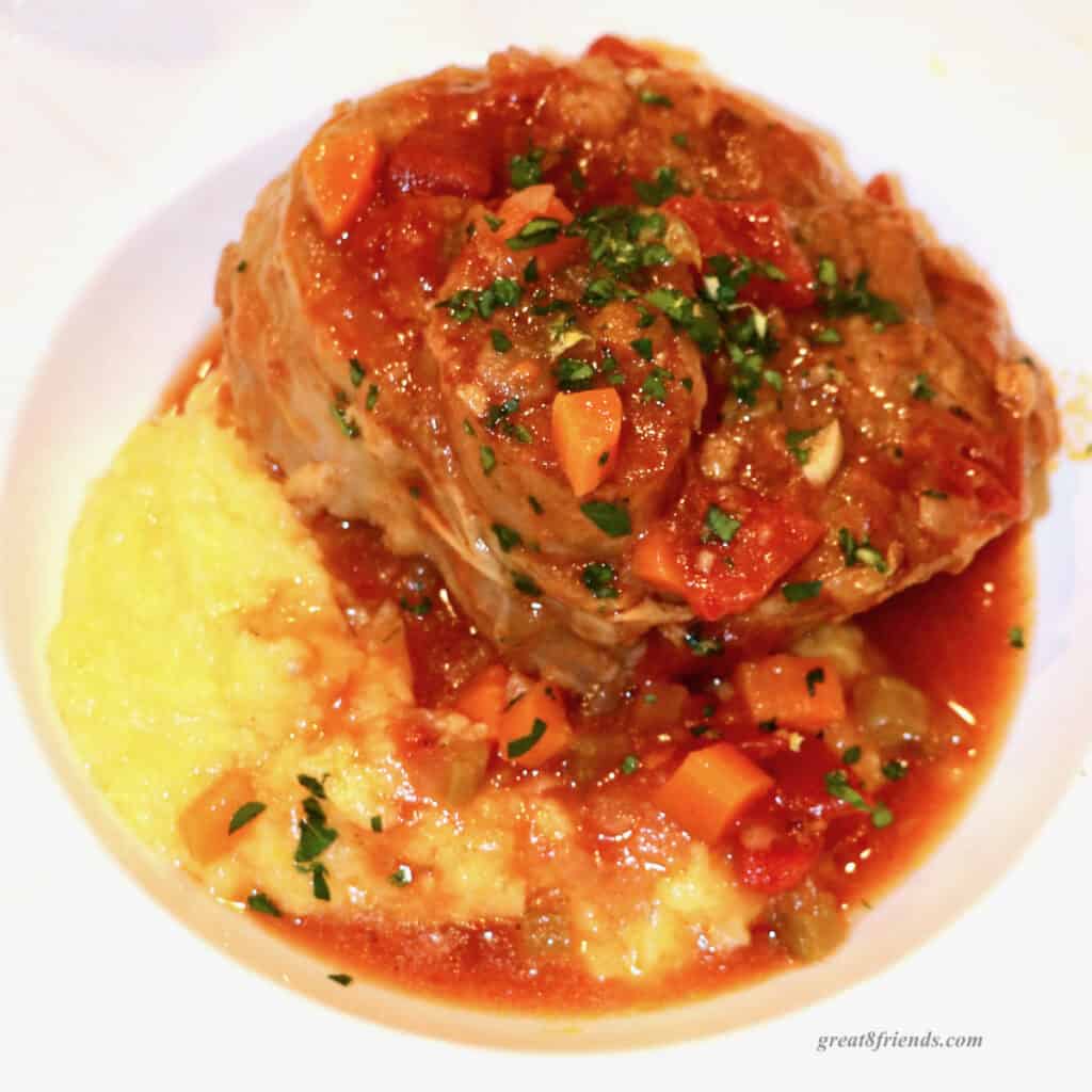 Osso buco on a bed of polenta in a white dish topped with gremolata.
