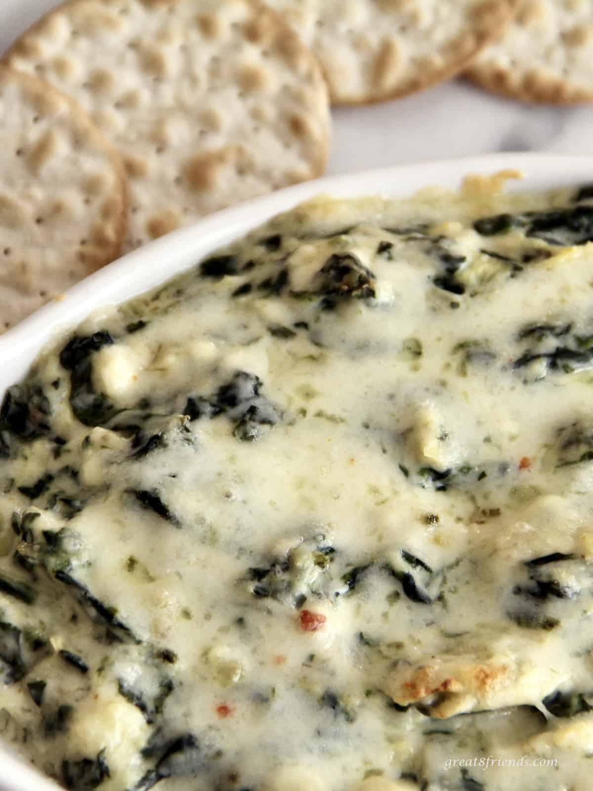 Upclose photo of a warm appetizer dip including spinach, artichokes and cheeses.