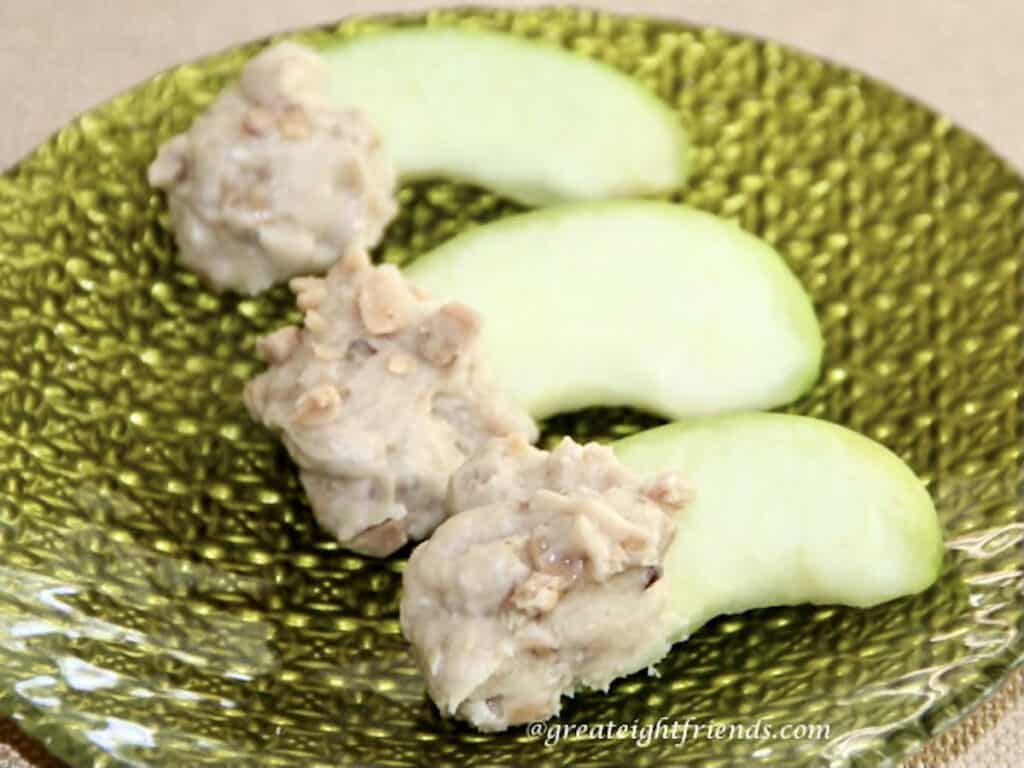 Three apple slices that have been dipped in a toffee cream cheese dip and being served on a green plate.