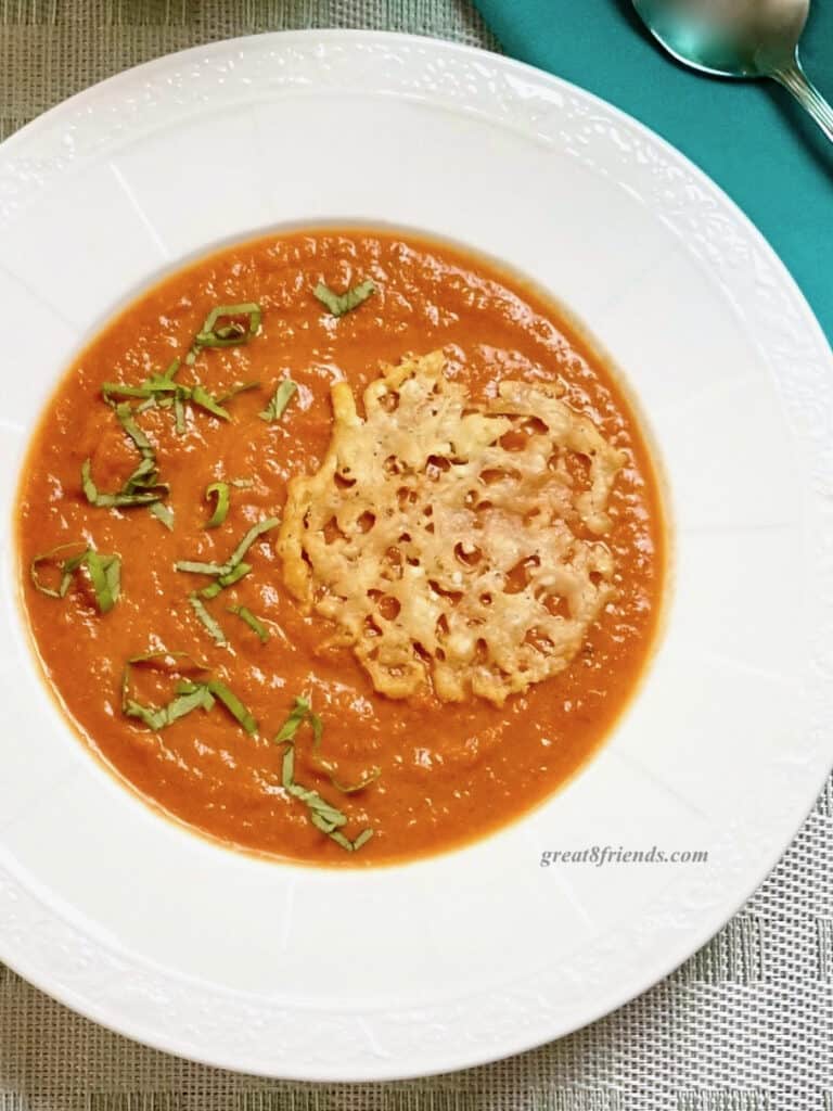 Overhead shot of tomato soup topped with basil and a parmesan crisp.