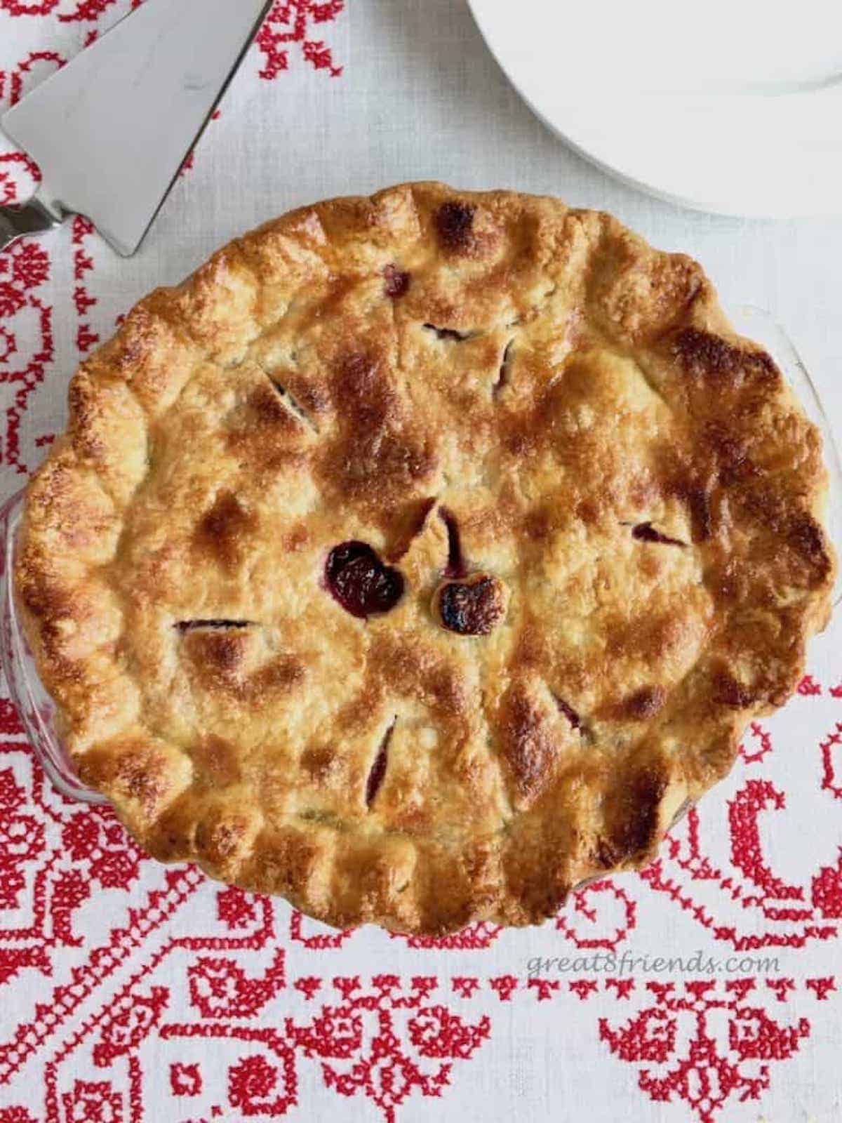 An overhead shot of a whole cherry pie on a red and white tablecloth.