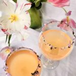 Overhead view of a pink lemonade margarita with edible flower bits on the edge of the glasses and a tulip plant next to the glasses.