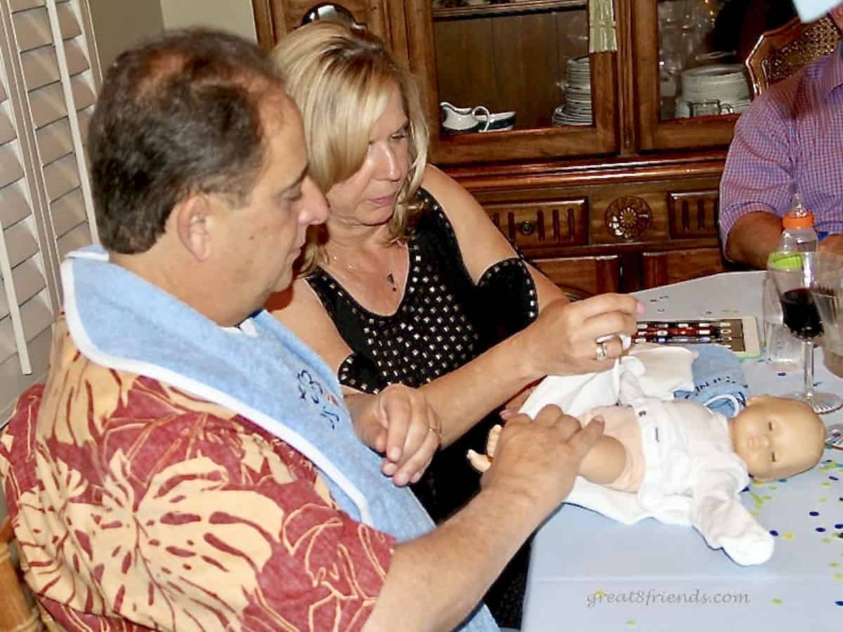 A man and a woman putting a diaper on a baby doll on a table.