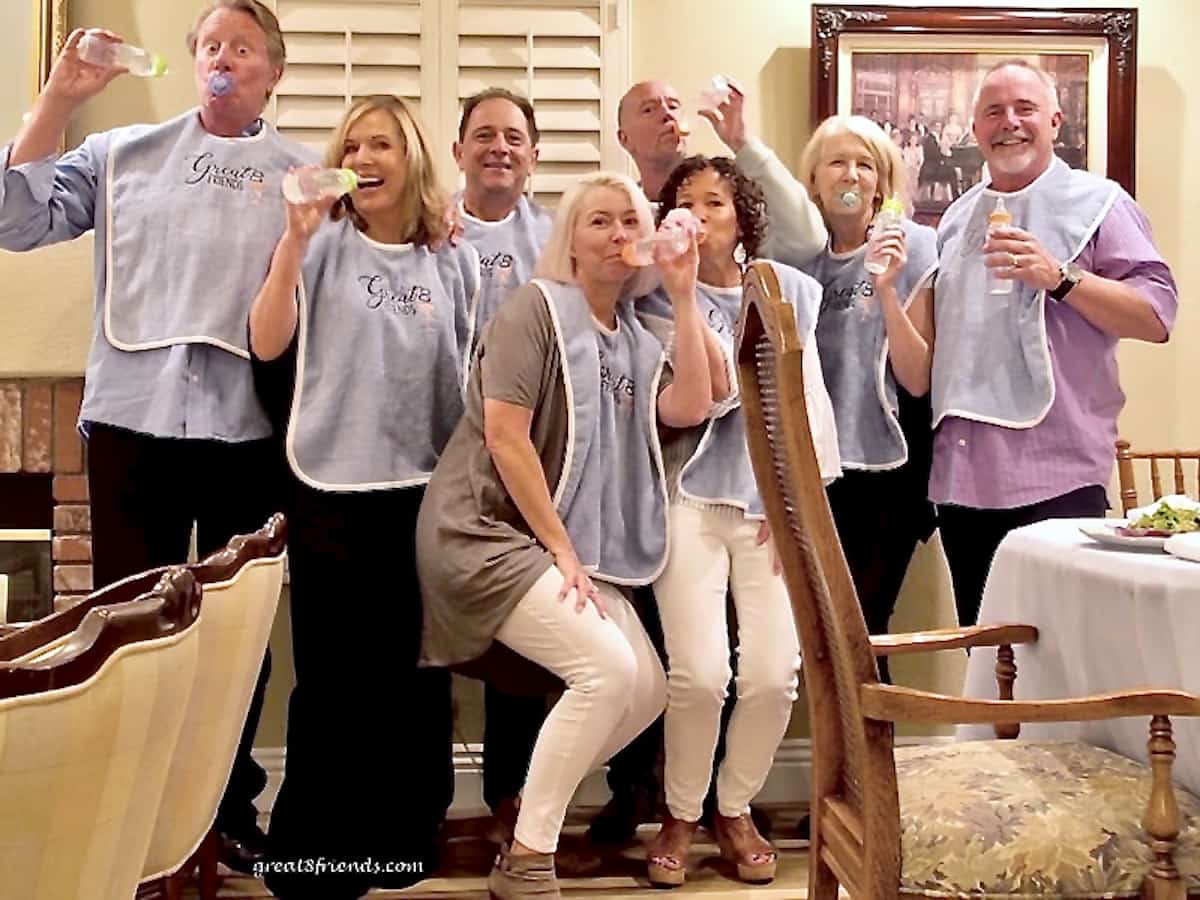 Eight people with adult bibs on and holding baby bottles and posing for the camera.