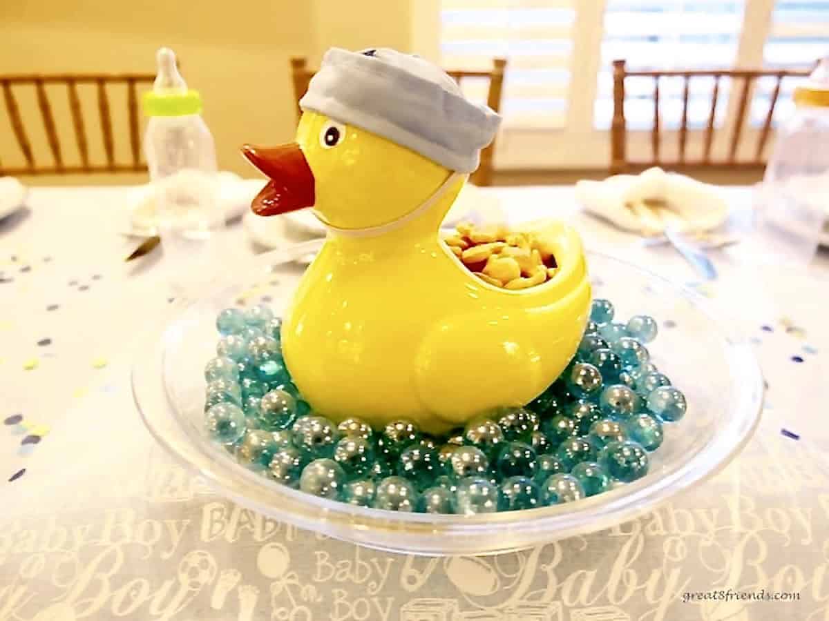 In the middle of a table, a large yellow duck sitting in a glass pie plate with blue glass marbles.